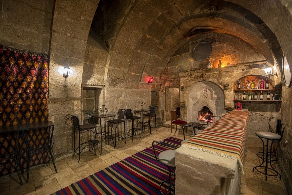 Una habitación acogedora con paredes de piedra, una mesa larga, taburetes de bar y una chimenea.