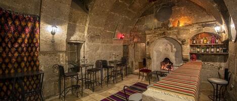 Una habitación acogedora con paredes de piedra, una mesa larga, taburetes de bar y una chimenea.