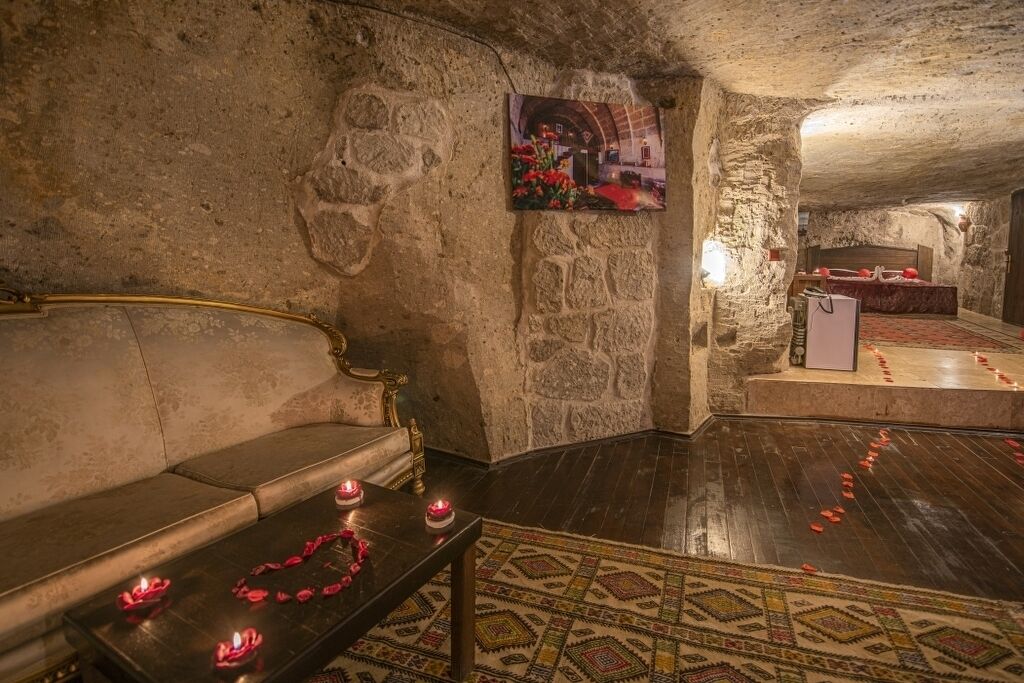 Habitación de paredes de piedra con un sofá, una mesita con velas y una cama adornada con pétalos de rosa.