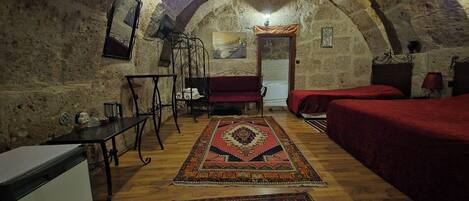 A rustic room with a vaulted ceiling, a bed, a sofa, a small table, and a chair.