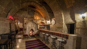 Zona de bar rústica con paredes de piedra, chimenea y taburetes de bar.
