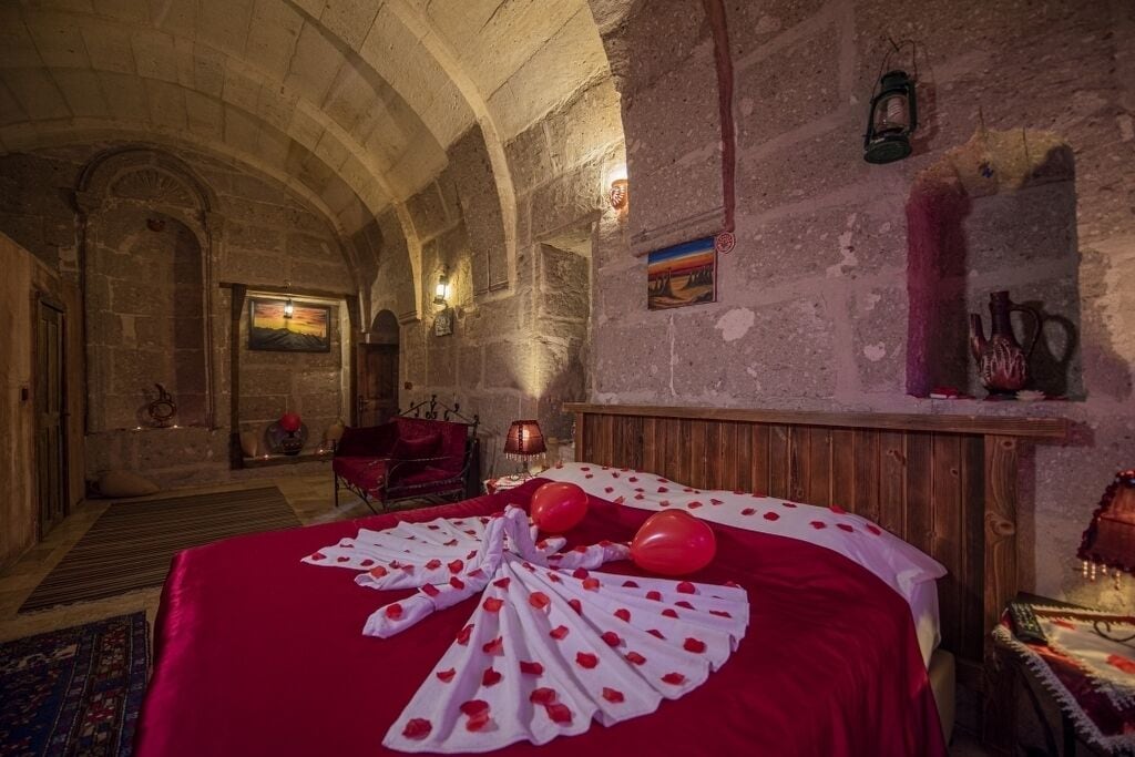 A room with a large bed, a wooden headboard, a red carpet, and a stone wall.