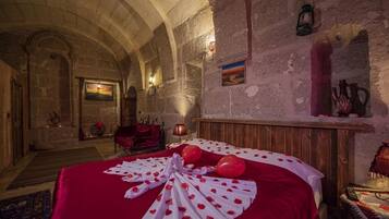 A room with a large bed, a wooden headboard, a red carpet, and a stone wall.