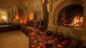 Una habitación acogedora con chimenea de piedra, una mesa adornada con pétalos de rosa y un sofá con cojines estampados.