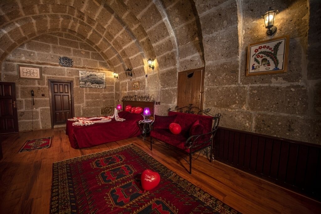 Una habitación acogedora con techo abovedado de piedra, un sofá rojo, una cama con manta roja y una alfombra estampada.