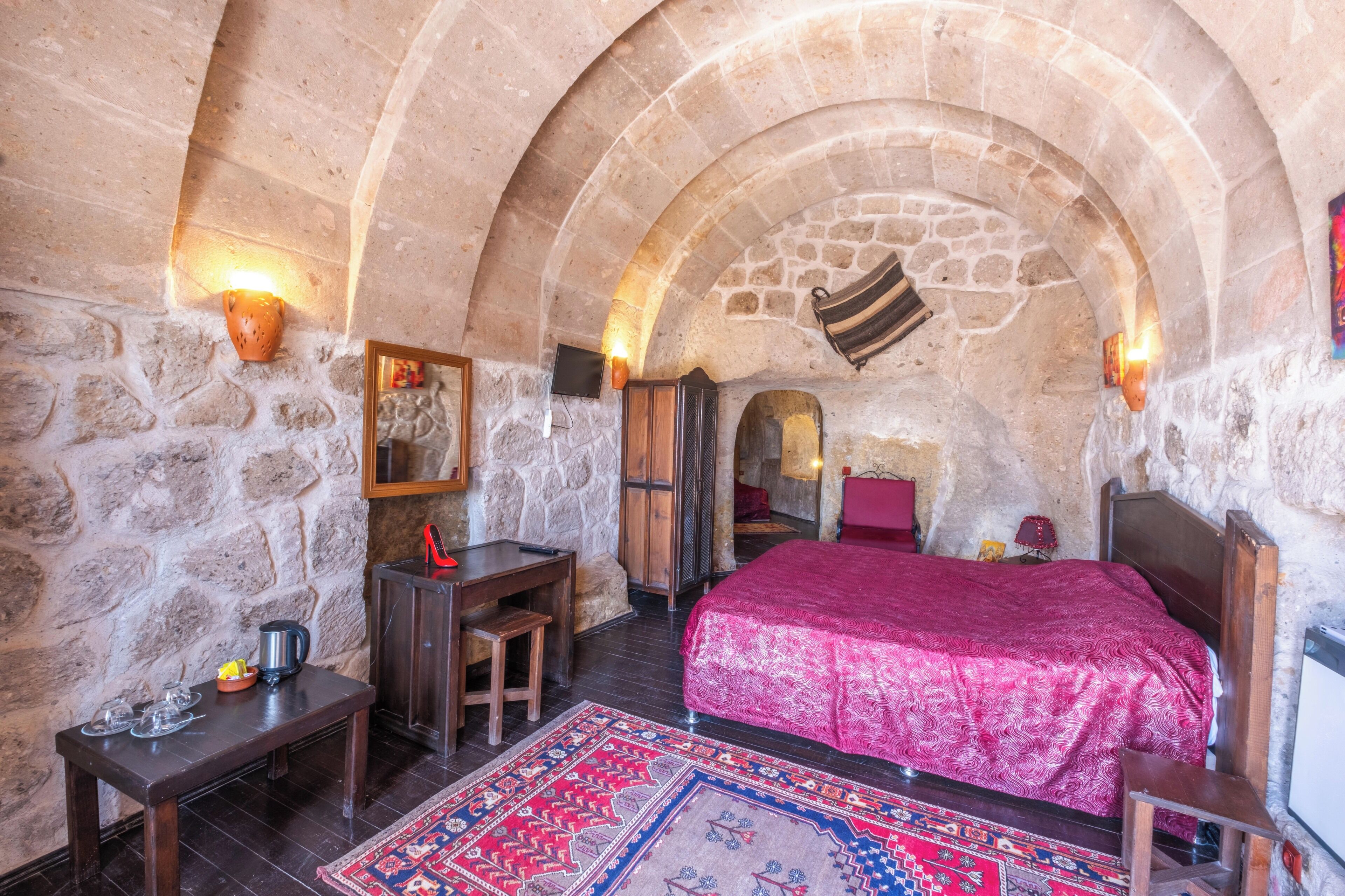A stone-walled room with a bed, a desk, and a television.