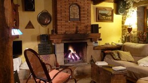 A cozy living room with a fireplace, a comfortable sofa, a wooden chair, and a television. - Casa Rural La Cortina (Cabrales)