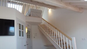 A bedroom with a white bed, a wooden staircase, and a white door with a window. - Casa Rural La Cortina (Cabrales)