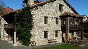 A stone building with a balcony and a wooden deck. - Casa Rural La Cortina (Cabrales)