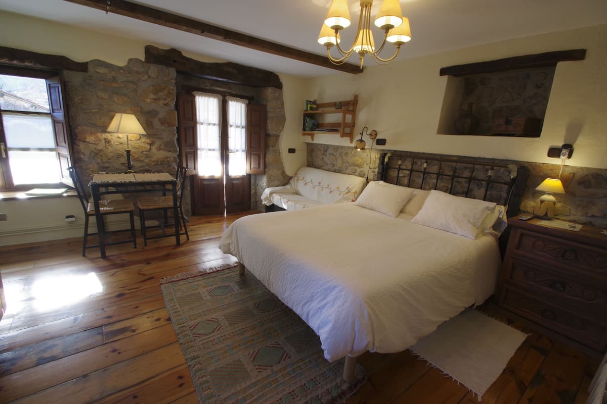 Un dormitorio con una cama grande, un aparador de madera, una pared de piedra y una araña.