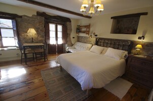 A bedroom with a large bed, a wooden dresser, a stone wall, and a chandelier.