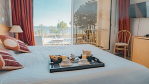 A hotel room with a bed, breakfast tray, and a balcony with a view. - Hôtel Edenia (Carnac)