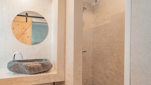 A bathroom with a stone sink, a round mirror, and a shower area. - Hôtel Edenia (Carnac)
