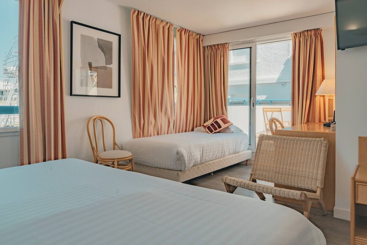 A hotel room with a bed, a chair, a desk, a lamp, and a framed picture on the wall.