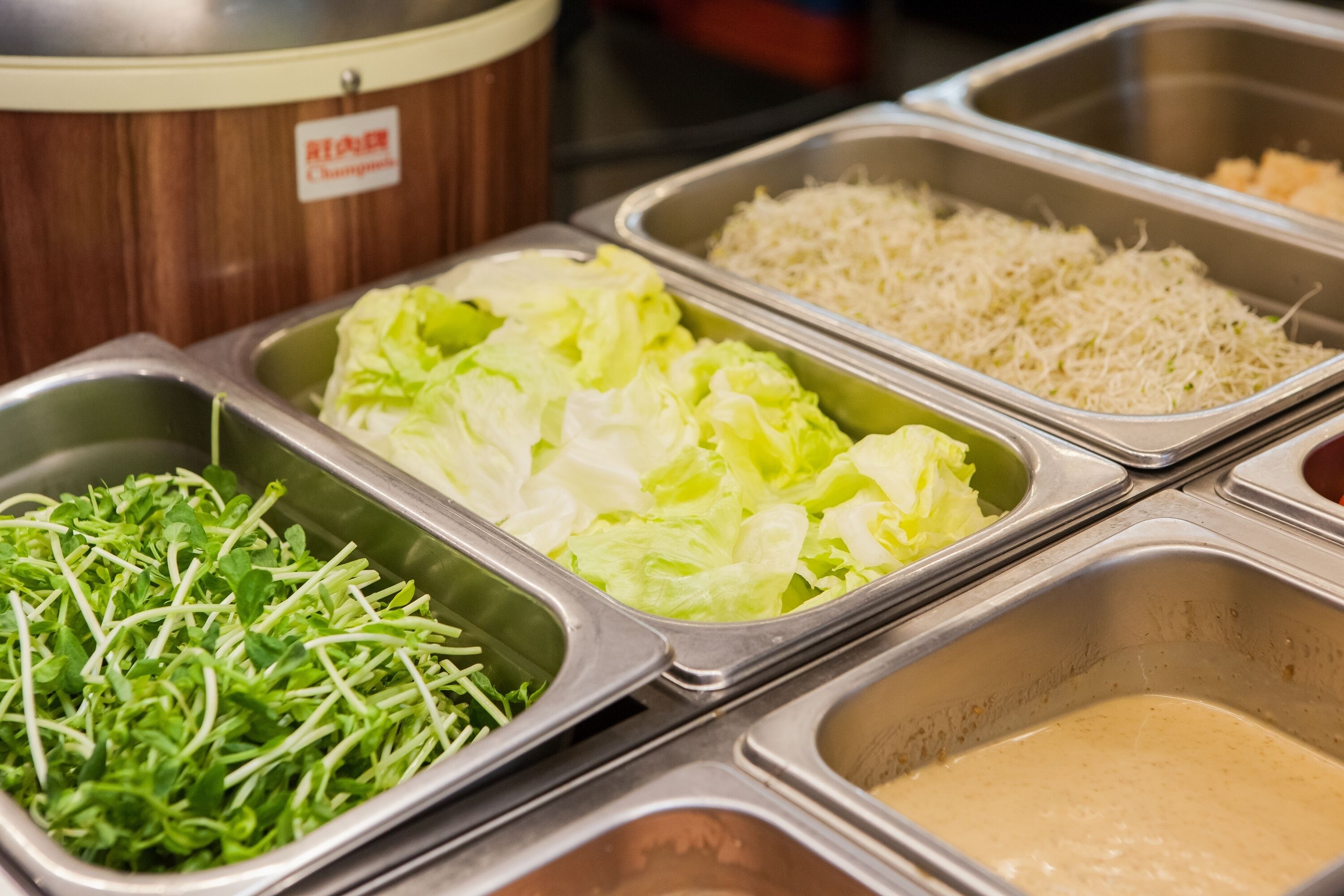 A buffet with various food options including greens, rice, and a creamy sauce.