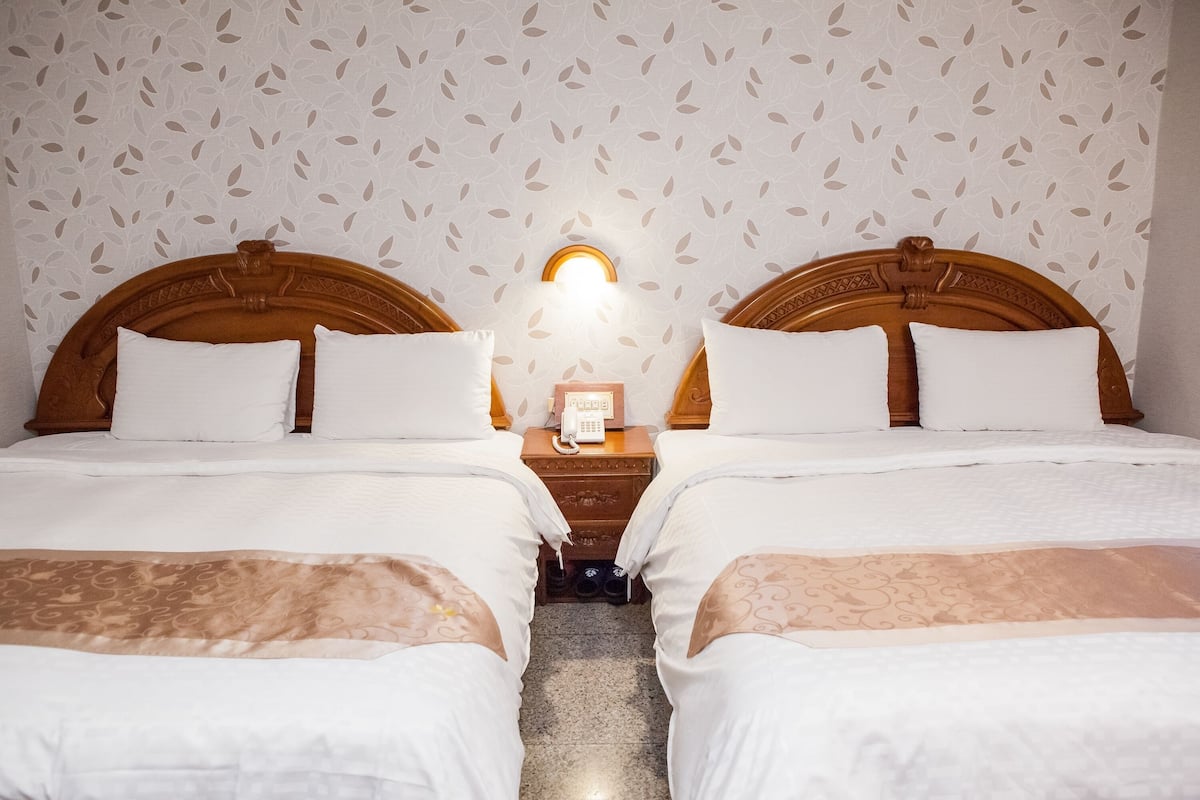 Een hotelkamer met twee bedden, een nachtkastje met een telefoon en behang met een patroon.