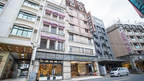A multi-story hotel with a modern facade, a covered entrance, and a visible parking area. - Mei Jia Mei Hotel (Jiaoxi)