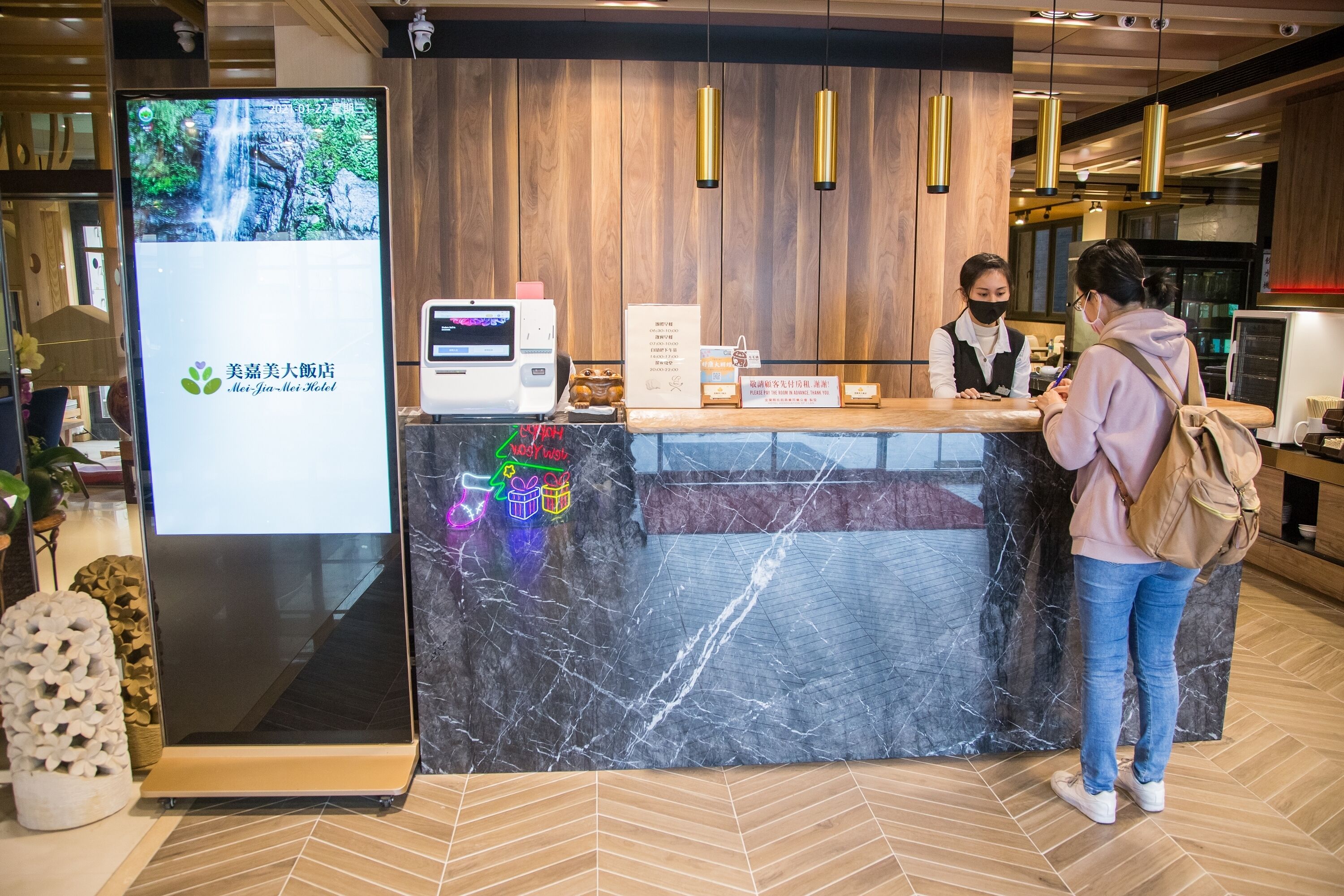 A hotel reception desk with a digital screen displaying a waterfall image, a cash register, and a menu board.