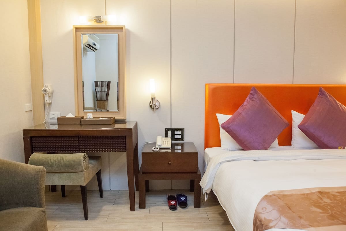 Een hotelkamer met een bed, nachtkastje, bureau, stoel en spiegel.