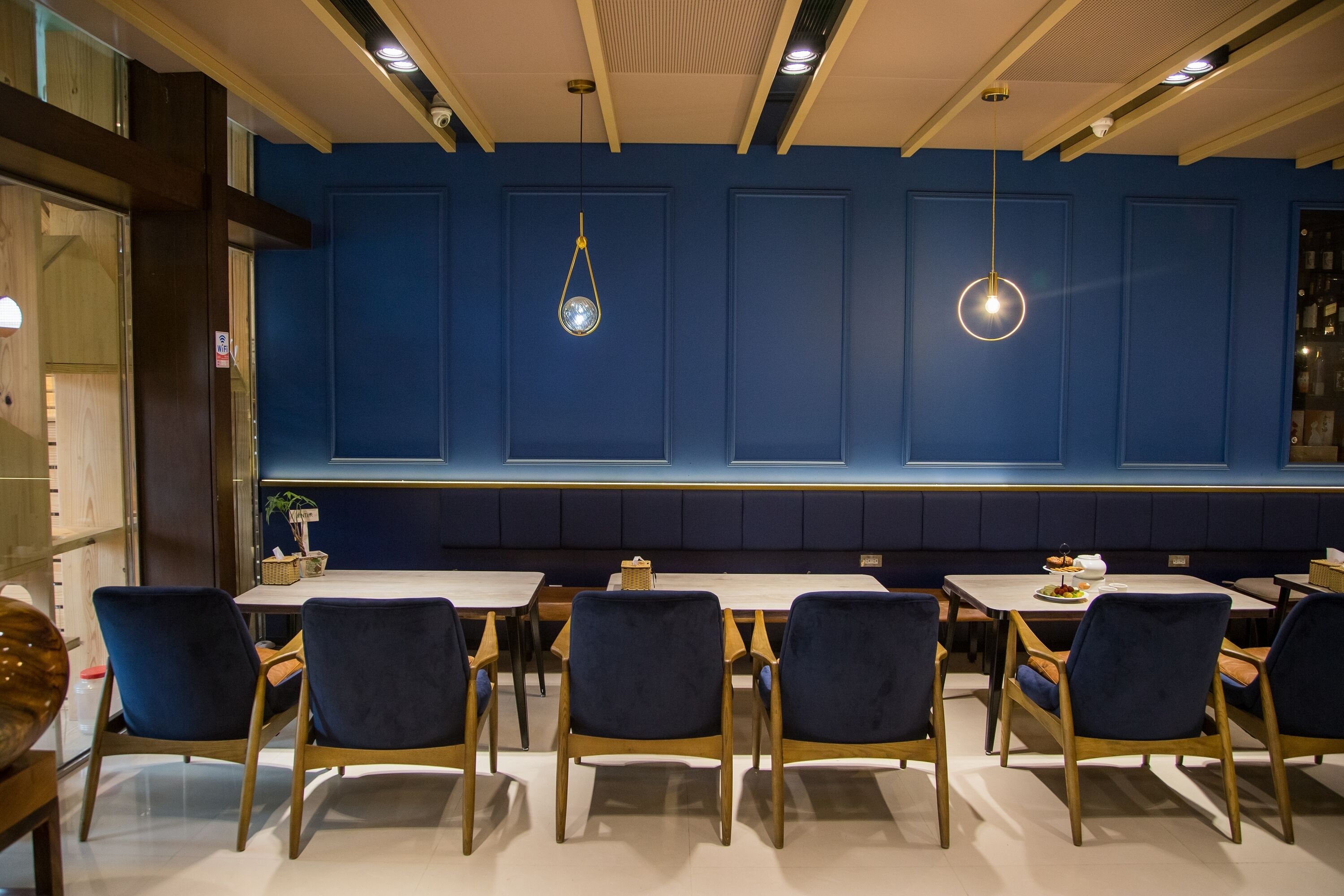 A dining area with blue paneled walls, wooden tables, and blue upholstered chairs.