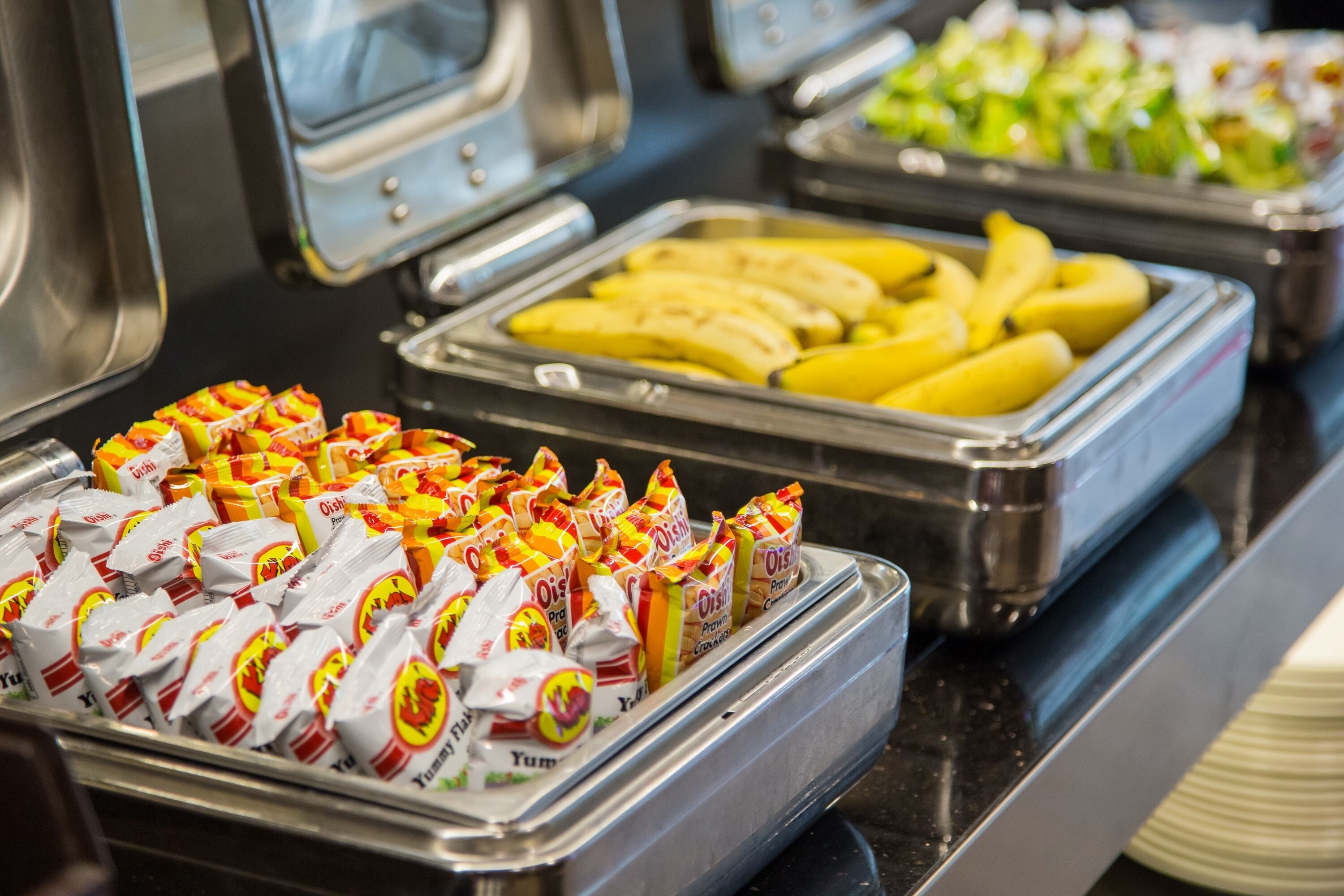 A buffet with various food items including bananas and packaged snacks.