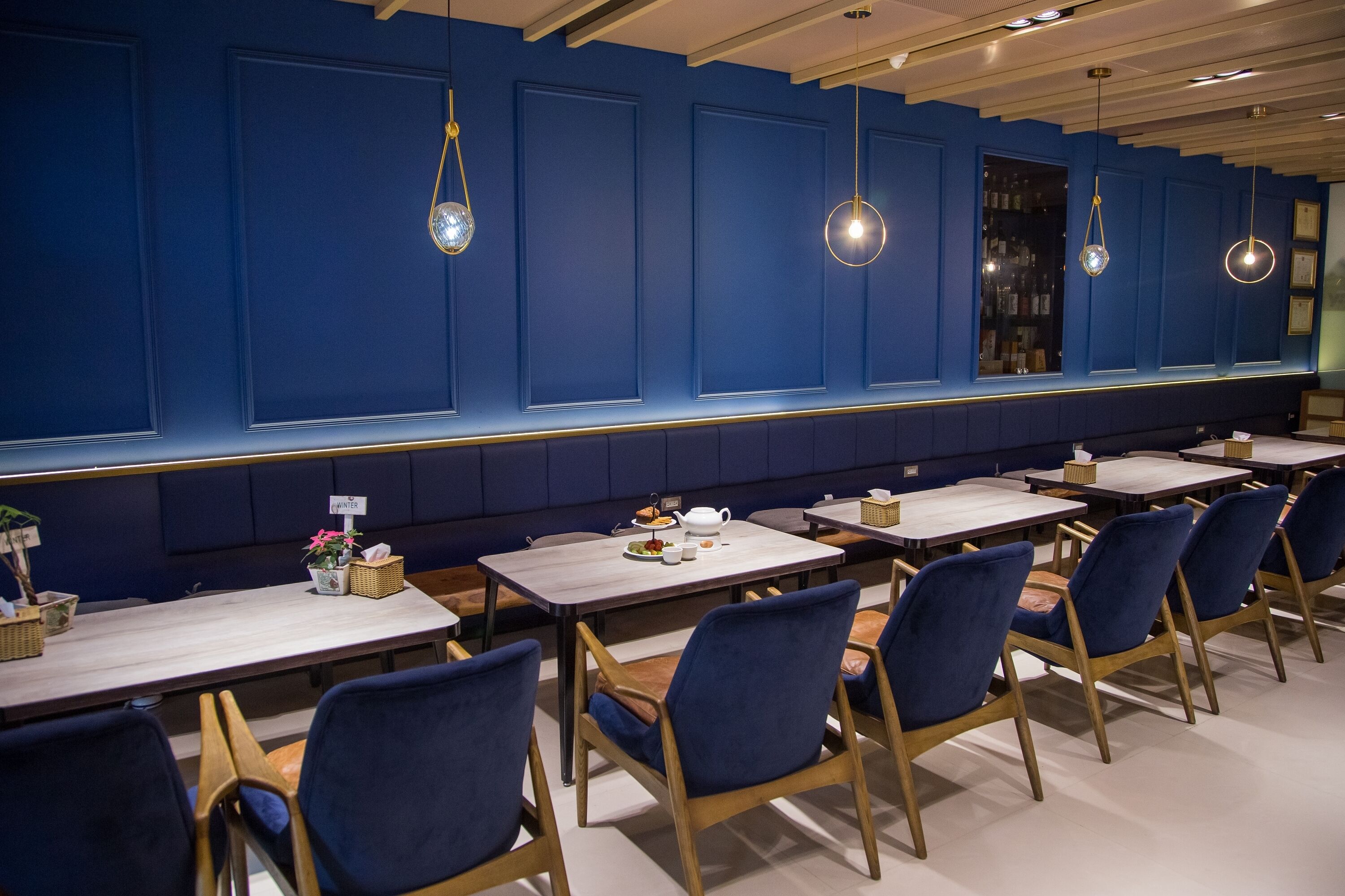 A restaurant with blue walls, wooden tables, and blue chairs.