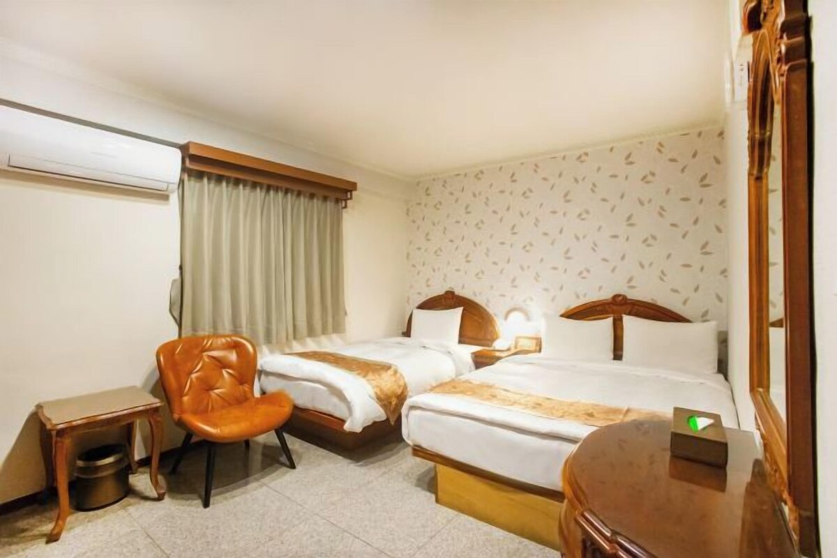 Habitació d'hotel amb dos llits, una cadira, una taula petita i un aparell d'aire condicionat.