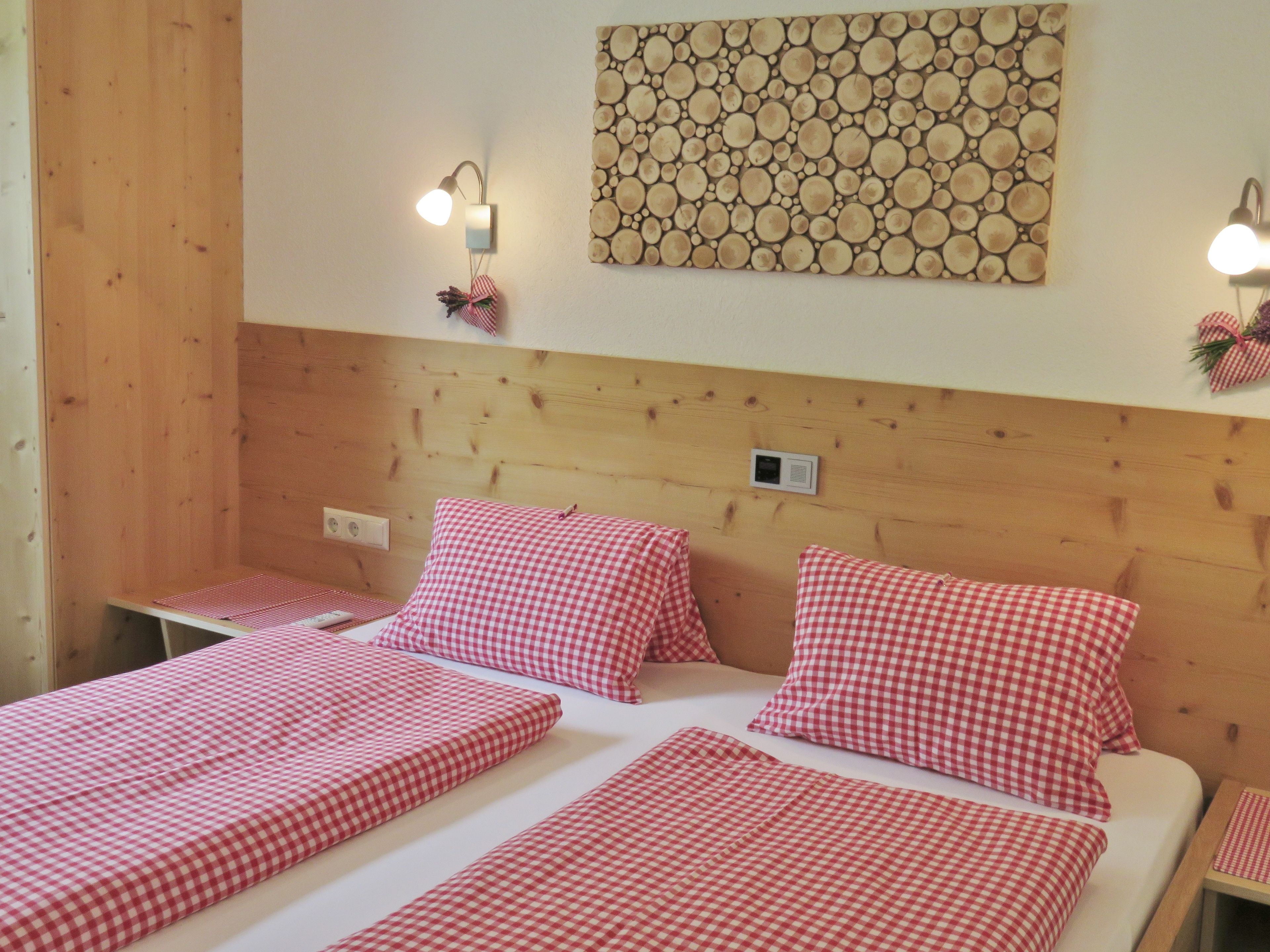 A room with wooden paneling, a bed with red and white checkered bedding, two bedside tables, and wall-mounted lights.