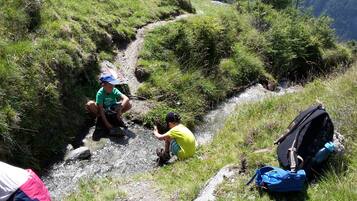 Two people near a stream in a grassy area with a backpack and a tent in the foreground.
