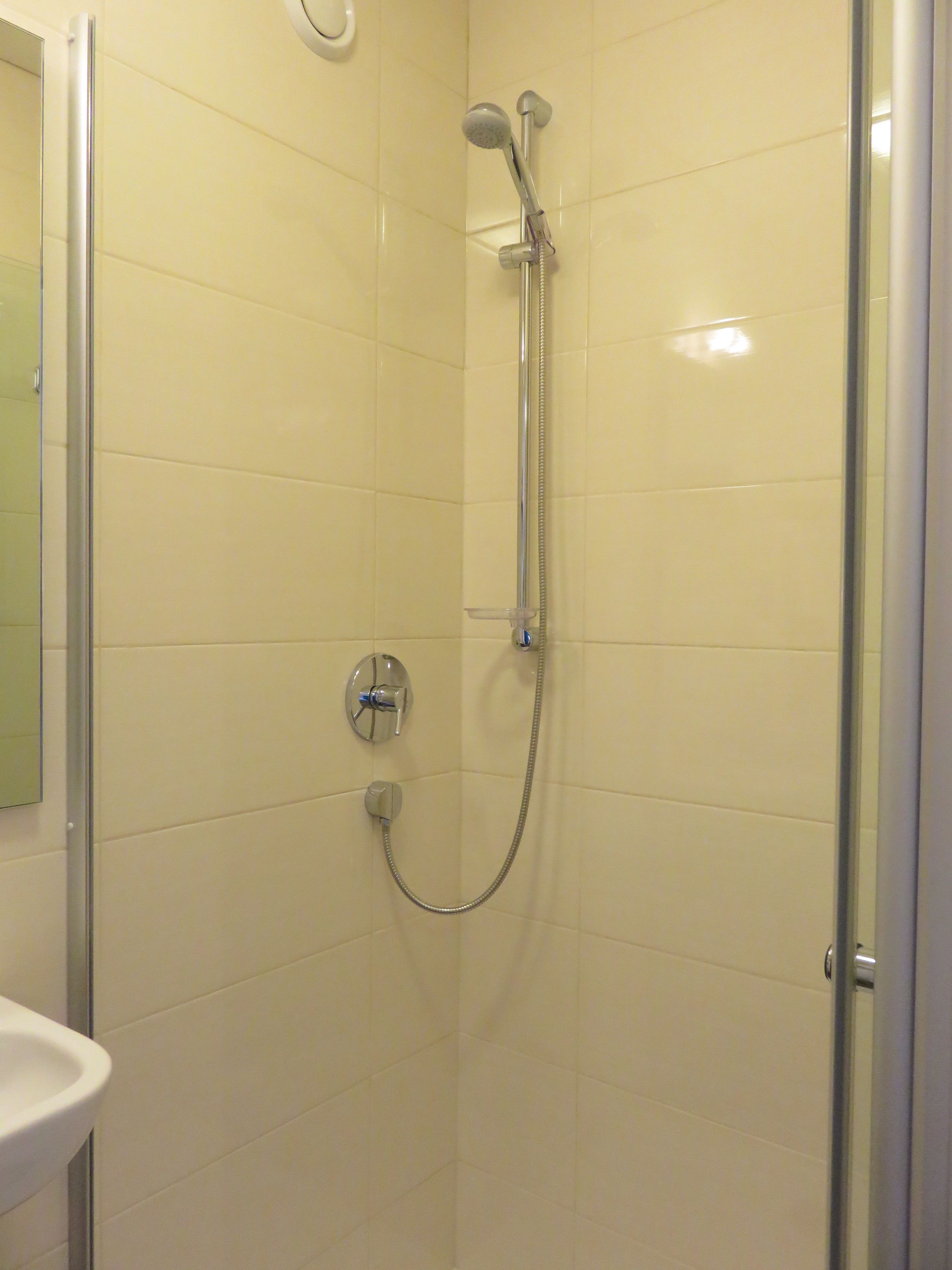 A shower with a handheld showerhead and a wall-mounted faucet, a glass shower door, and a white sink to the left.