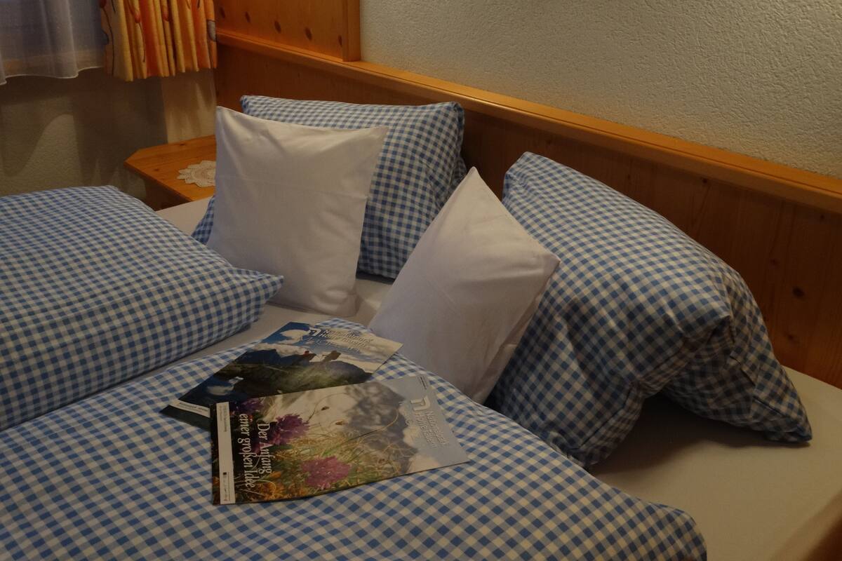 Quarto de hotel com cabeceira de madeira, roupa de cama xadrez e um livro sobre a cama.