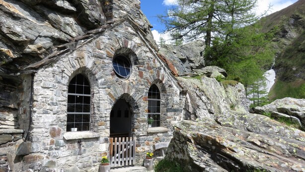 A stone building with arched windows and a wooden door, surrounded by rocks and trees. - Zedlacherhof (Matrei in Osttirol)