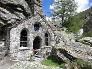 A stone building with arched windows and a wooden door, surrounded by rocks and trees. - Zedlacherhof (Matrei in Osttirol)