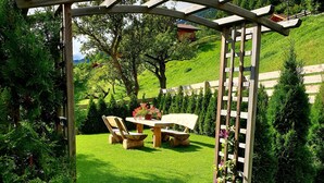 A wooden pergola with a table and chairs in a lush garden. - Zedlacherhof (Matrei in Osttirol)