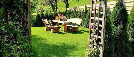 A wooden pergola with a table and chairs in a lush garden.