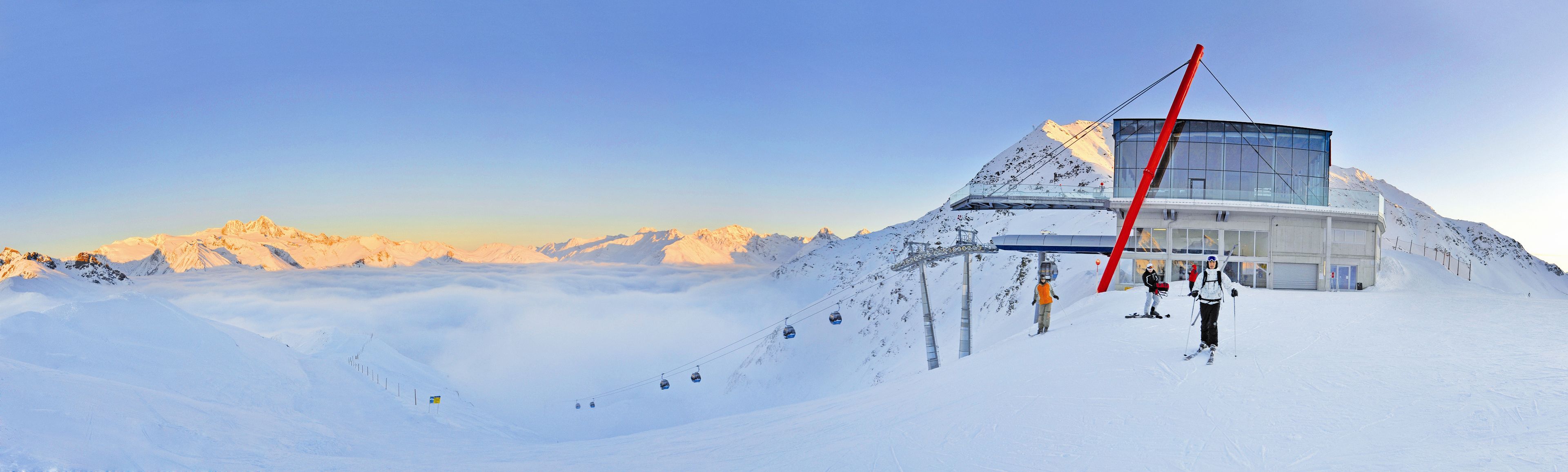 Ein schneebedeckter Berg mit einer Seilbahn und einem modernen Gebäude mit großen Fenstern.