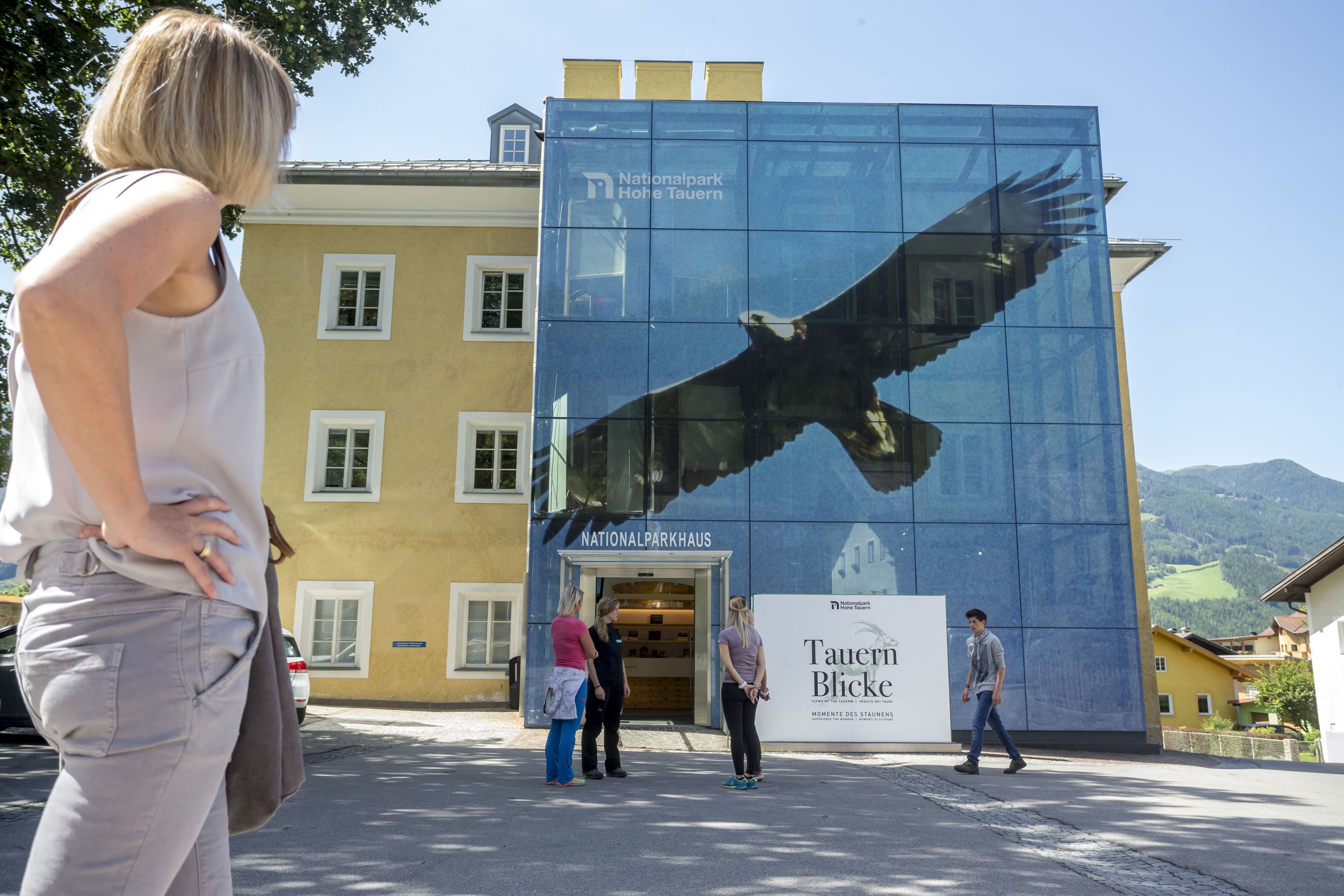 Un edificio con un amplio muro de cristal que presenta un mural de aves, un letrero que dice Nationalpark Home Tauern y un letrero que dice Tauer Blicke.