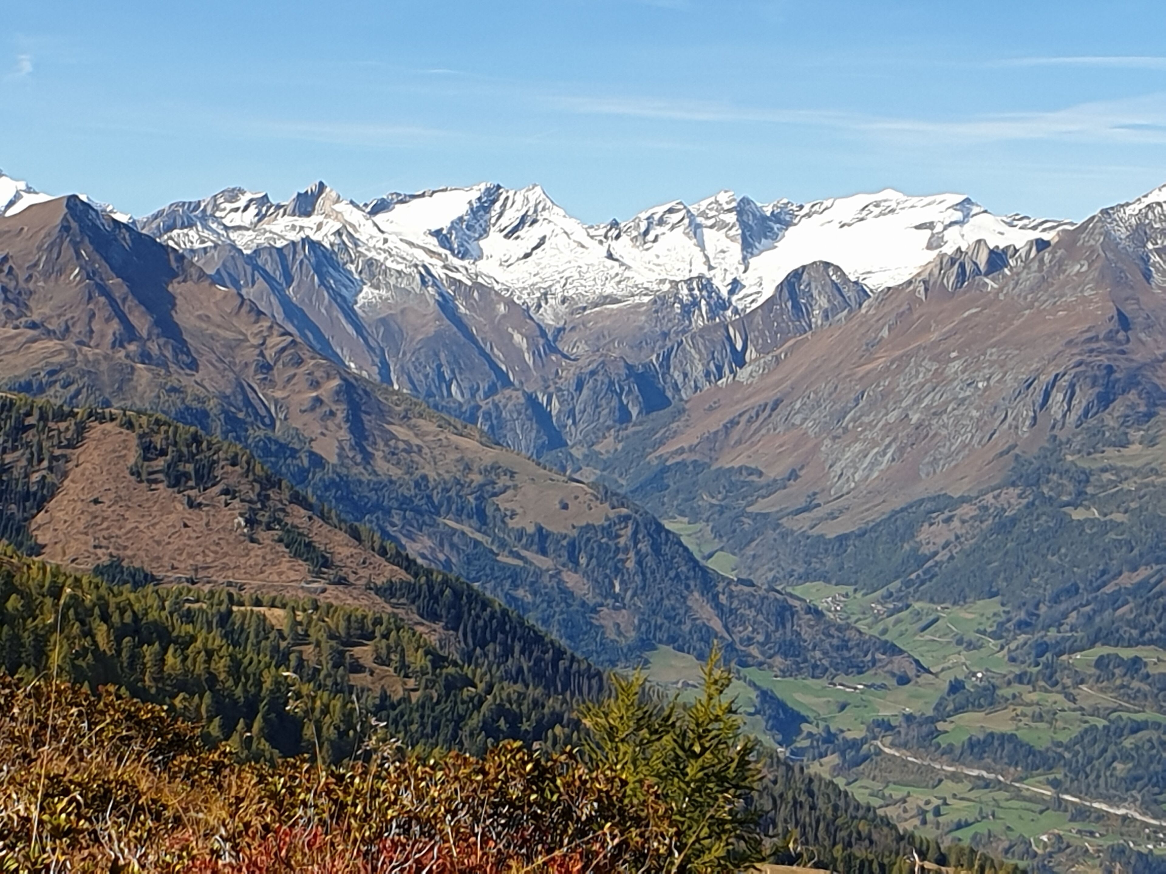 A mountainous landscape with snow-capped peaks and a valley with green fields.