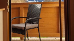 A balcony with a wicker chair, a wooden floor, and a view of snow-covered mountains. - Zedlacherhof (Matrei in Osttirol)