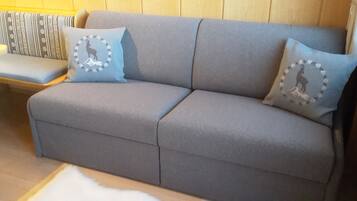 Ein graues Sofa mit zwei passenden Kissen, eine Bank und ein flauschiger, weißer Teppich.