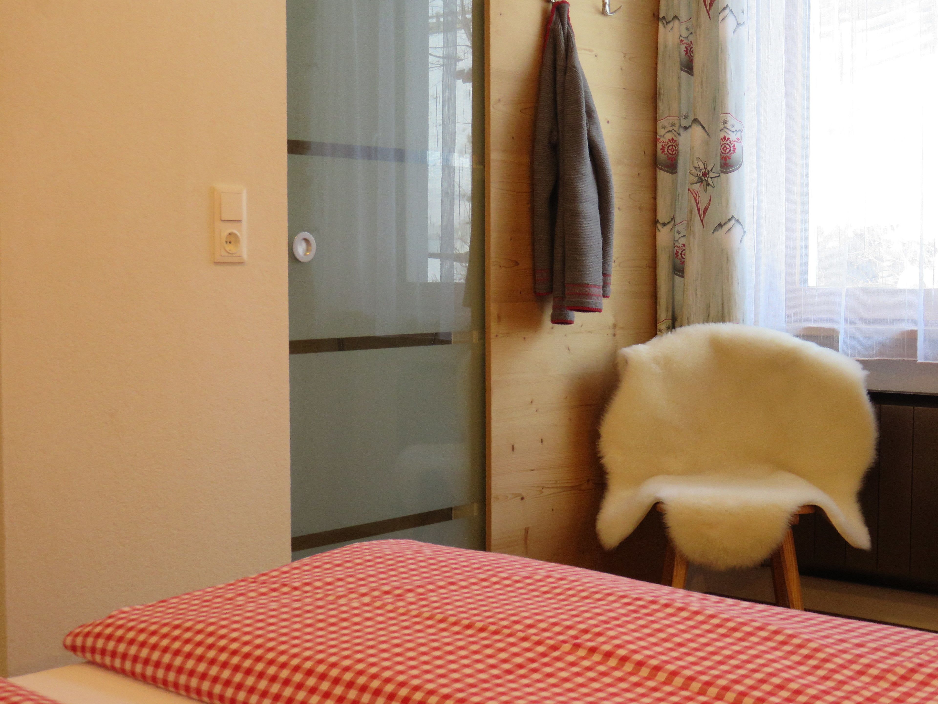 Un dormitori amb un llençol estriat, una cadira blanca, una porta de fusta i una finestra amb cortines.