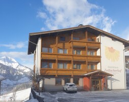 Un hotel de varios pisos con fachada de madera, un automóvil estacionado al frente y paisajes nevados a su alrededor.