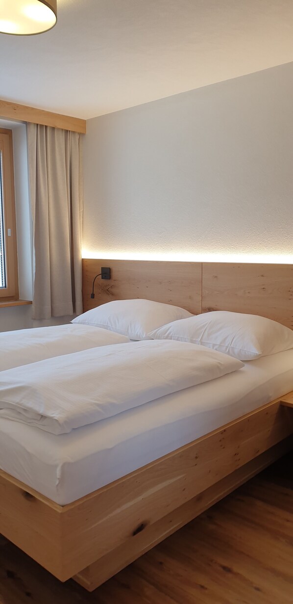 A wooden bed with white bedding in a room with a wooden headboard and a bedside lamp. - Zedlacherhof (Matrei in Osttirol)