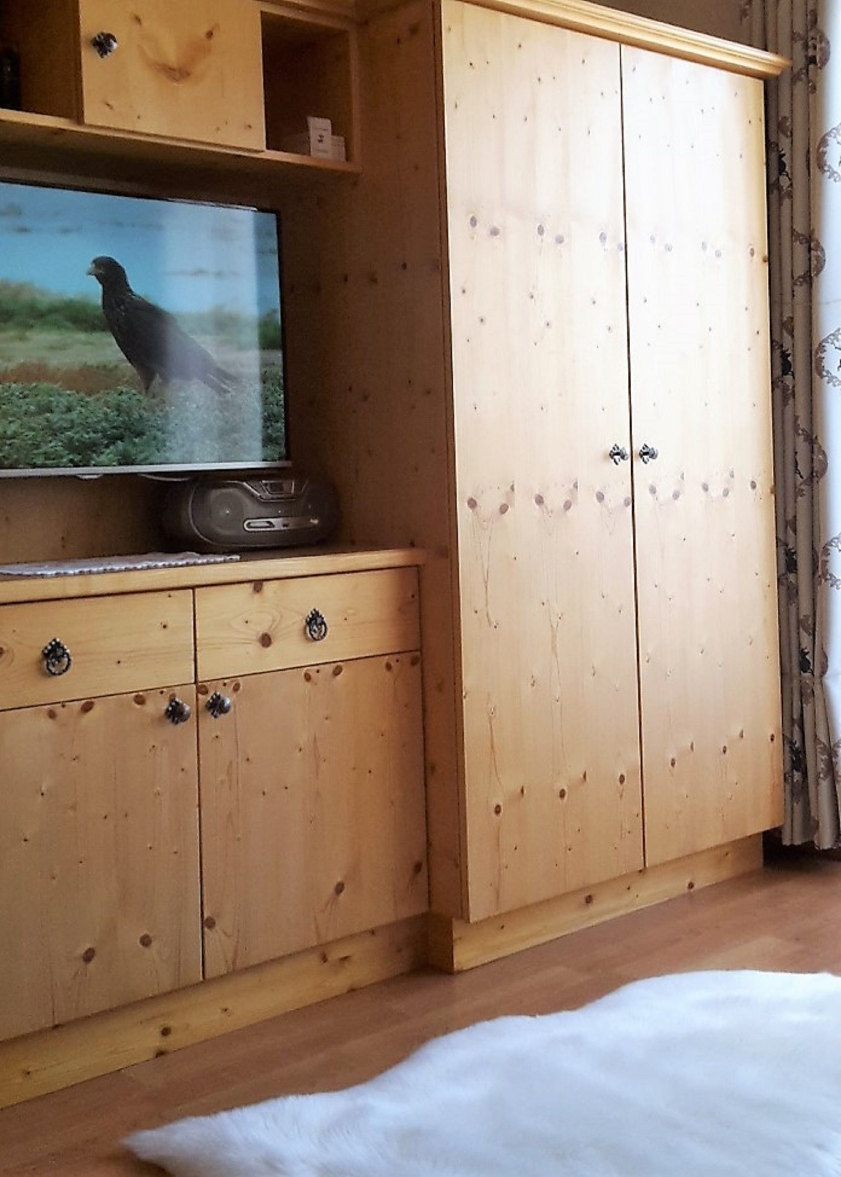A wooden cabinet with a television on top, a white rug, and a wooden floor.