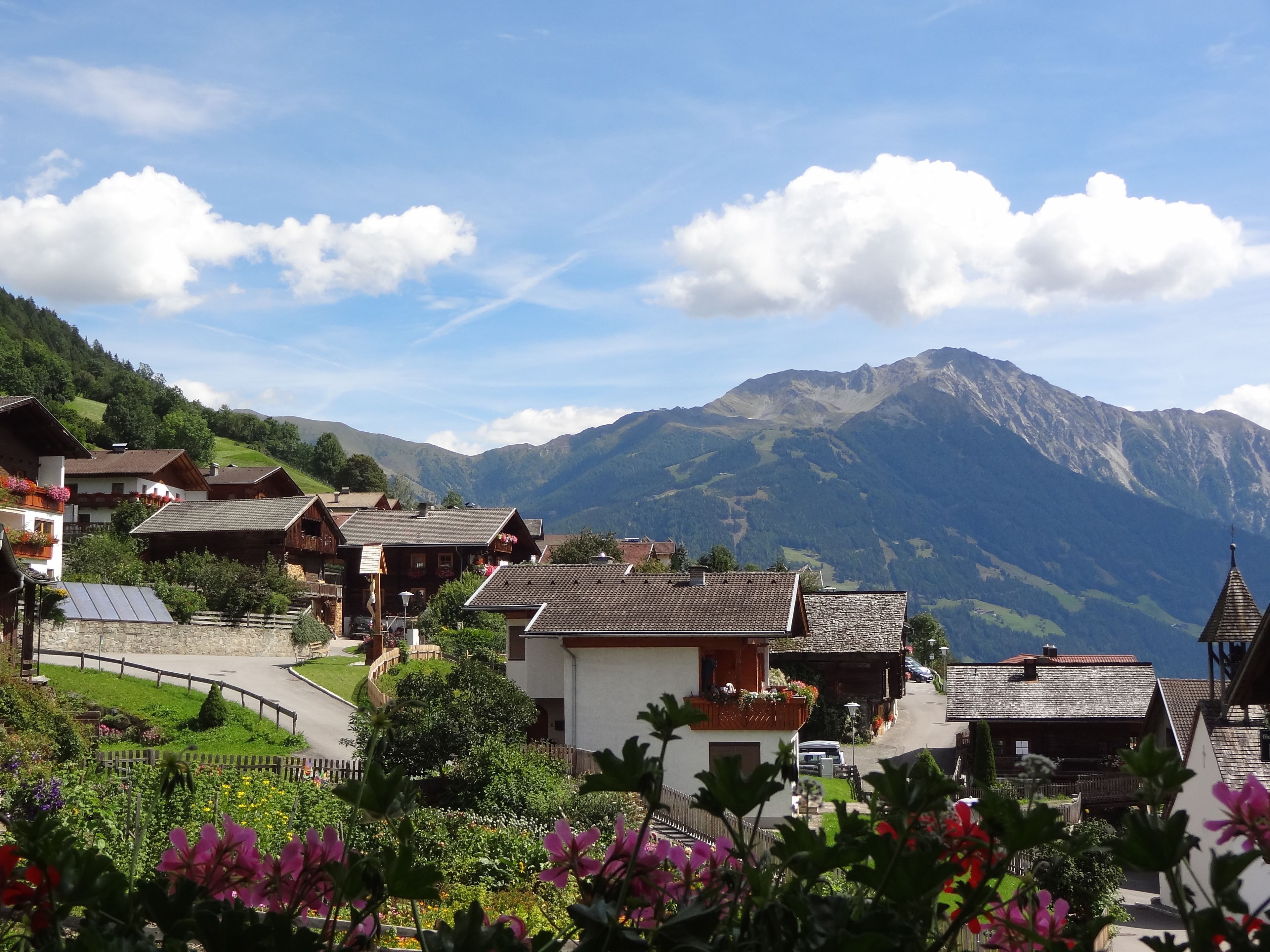 Un pueblo de montaña con casas de madera tradicionales, un camino sinuoso y vistas de las montañas circundantes.