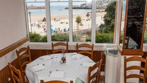 A dining area with a table set for four, overlooking a beach with people and umbrellas. - Hostal Buenavista (Cervo)