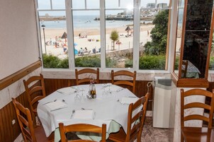 Un comedor con una mesa dispuesta para cuatro personas, con vistas a una playa con gente y sombrillas.