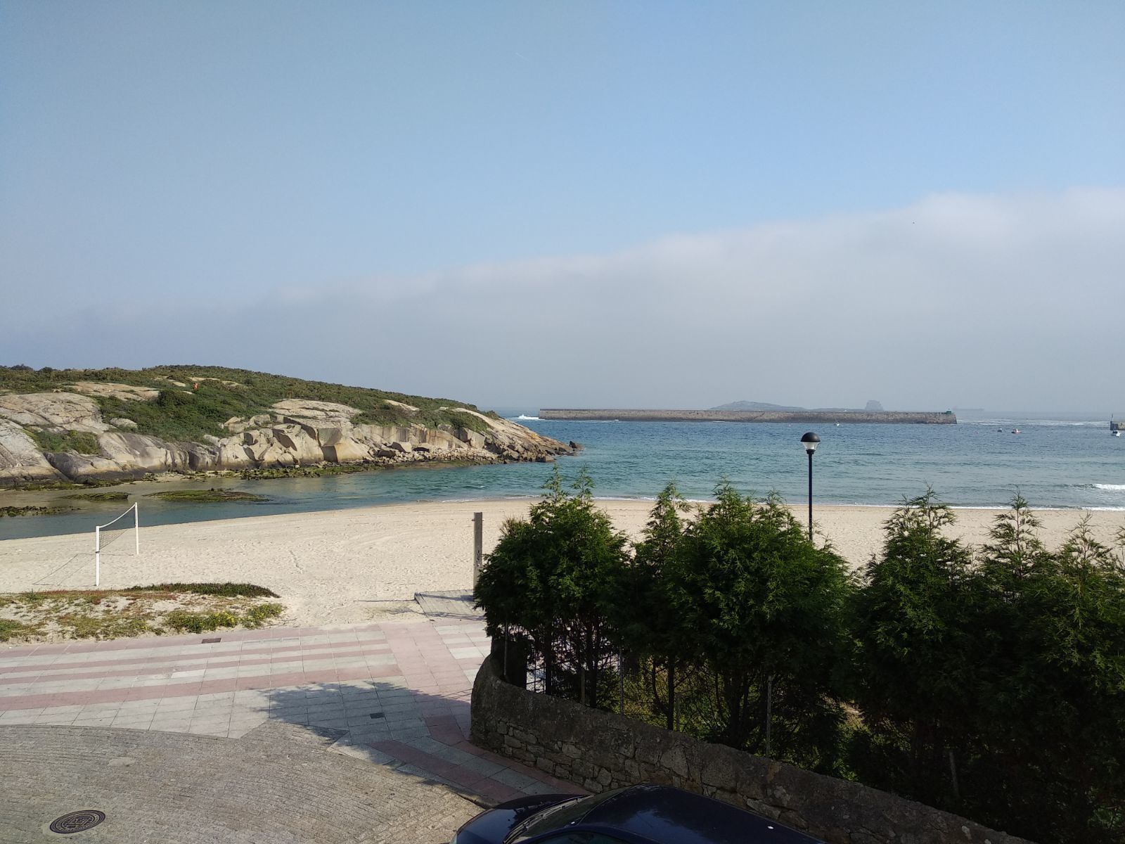 Uitzicht op de kust met een zandstrand, een stenen muur en een heldere lucht.