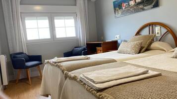 A hotel room with two beds, a desk, a chair, and a painting on the wall.