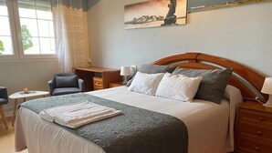 A neatly arranged hotel room with a large bed, a desk, a chair, and a small table. - Hostal Buenavista (Cervo)